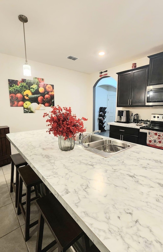 kitchen featuring sink, light tile patterned floors, a breakfast bar area, appliances with stainless steel finishes, and decorative light fixtures