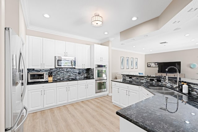 kitchen with stainless steel appliances, white cabinets, light wood-style floors, and dark stone countertops