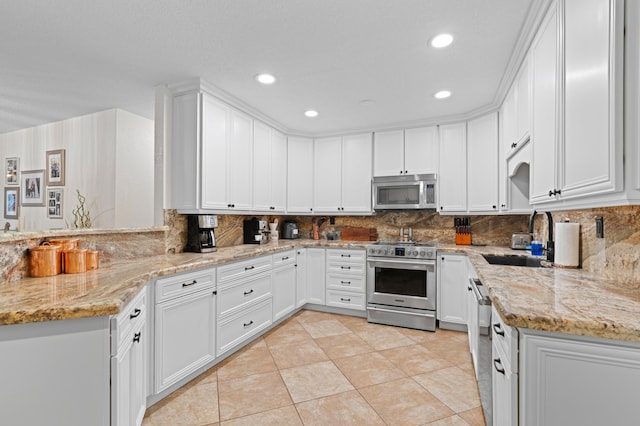 812 NW 26th St, Wilton Manors, FL 33311 - kitchen with stainless steel appliances, a sink, backsplash, white cabinetry, and light stone counters