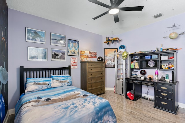 bedroom with a ceiling fan, wood finished floors, visible vents, and baseboards