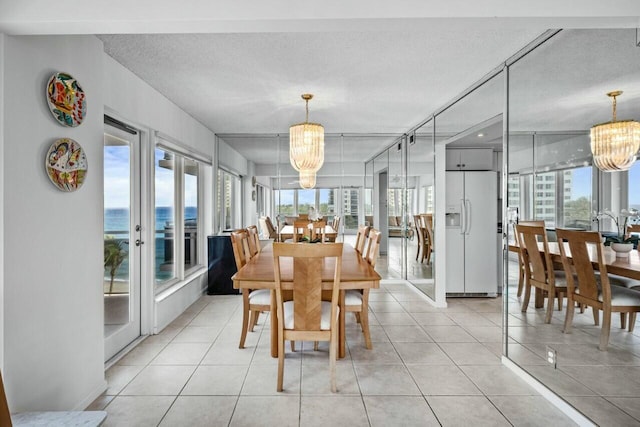 dining area featuring a water view, light tile patterned floors, a textured ceiling, and a notable chandelier