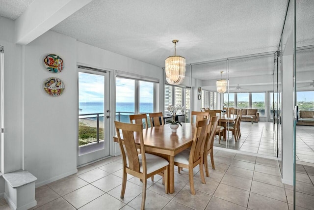 dining area with a water view, light tile patterned flooring, a textured ceiling, and a notable chandelier