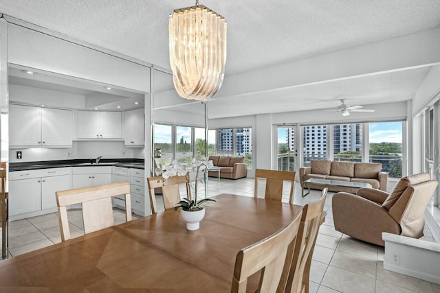 tiled dining space with sink, ceiling fan with notable chandelier, and a textured ceiling