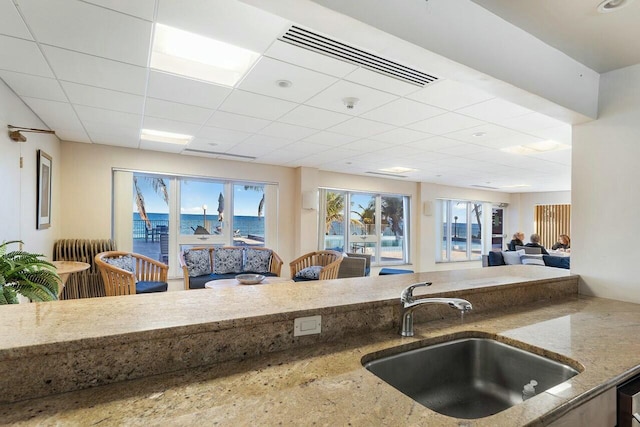 kitchen with a water view, stone countertops, sink, and a drop ceiling