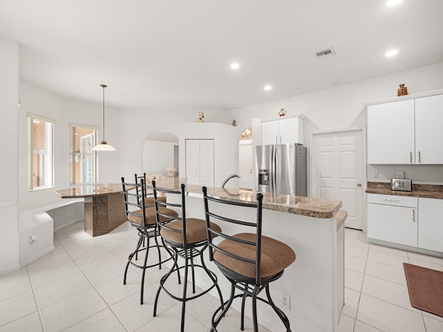 kitchen with decorative light fixtures, white cabinets, stainless steel fridge, light tile patterned floors, and a center island with sink