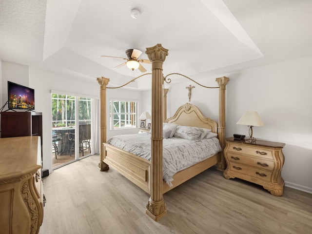 bedroom featuring access to exterior, a raised ceiling, light hardwood / wood-style floors, and a textured ceiling