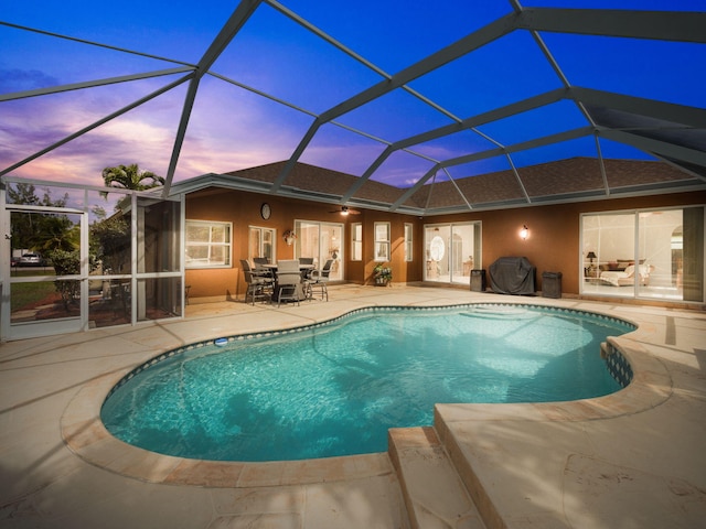 pool at dusk with a patio area, ceiling fan, and glass enclosure