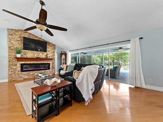 living room with ceiling fan, a stone fireplace, vaulted ceiling, and light wood-type flooring