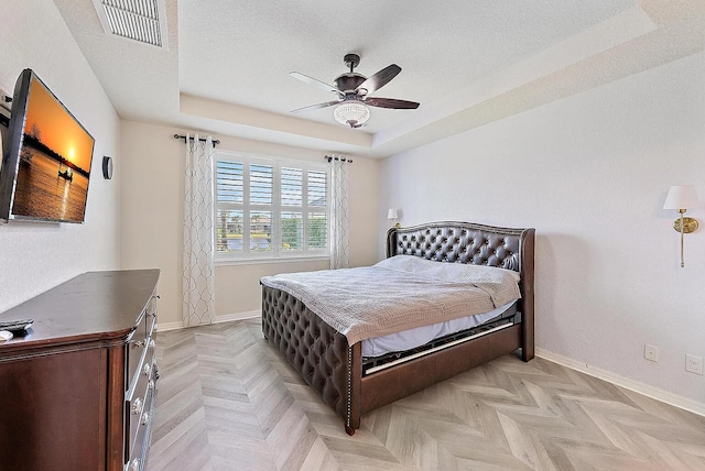 bedroom with light parquet flooring, ceiling fan, a textured ceiling, and a tray ceiling