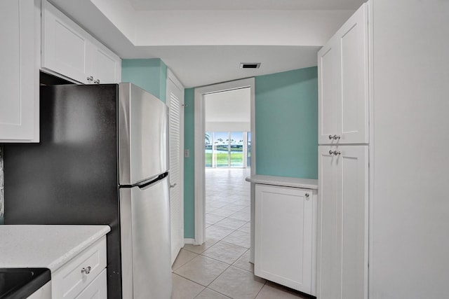 kitchen featuring stainless steel refrigerator, light tile patterned flooring, and white cabinets