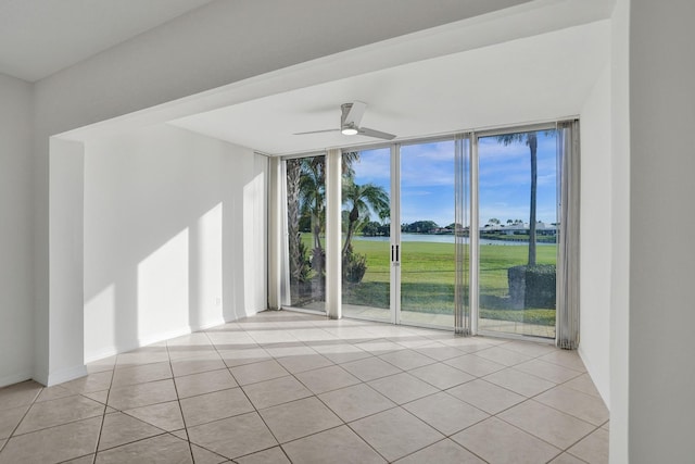 tiled empty room with a water view, expansive windows, a ceiling fan, and baseboards