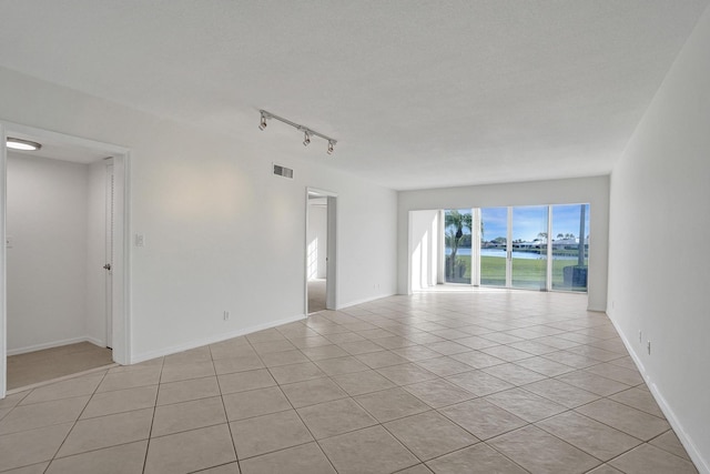 unfurnished room featuring light tile patterned floors, a water view, track lighting, and baseboards