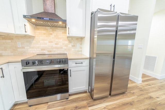 kitchen with white cabinetry, electric range oven, exhaust hood, and stainless steel refrigerator