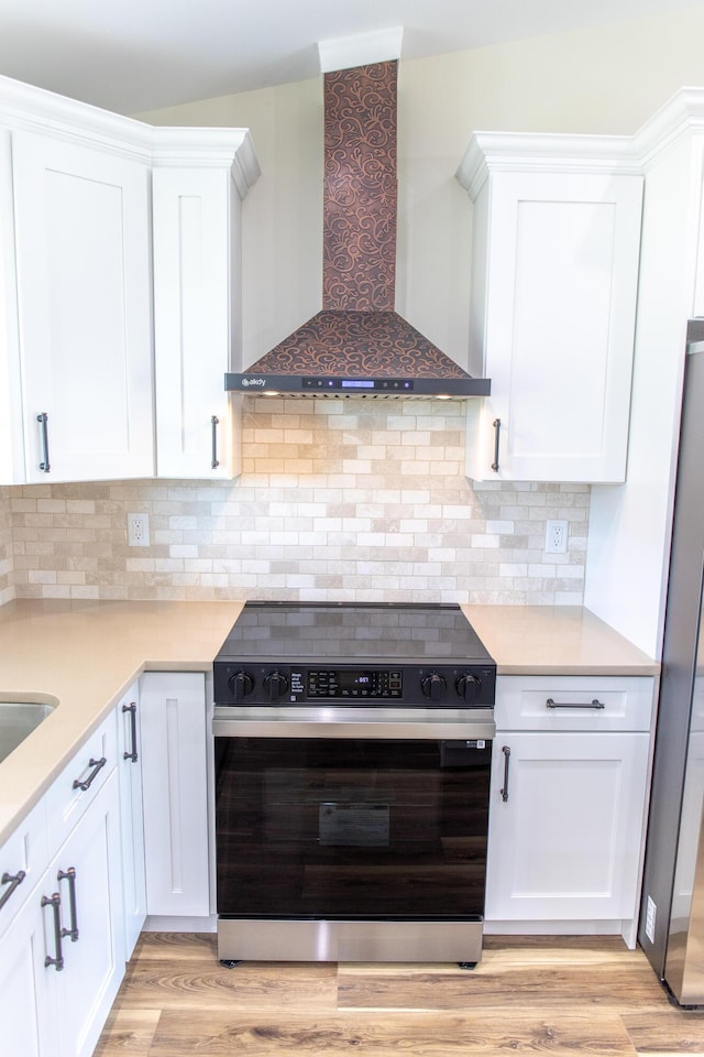 kitchen with wall chimney exhaust hood, electric range oven, light wood-type flooring, stainless steel refrigerator, and white cabinets