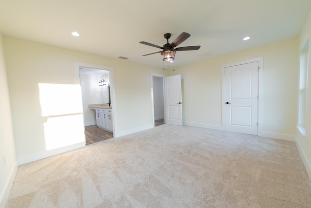 unfurnished bedroom featuring connected bathroom, light carpet, and ceiling fan