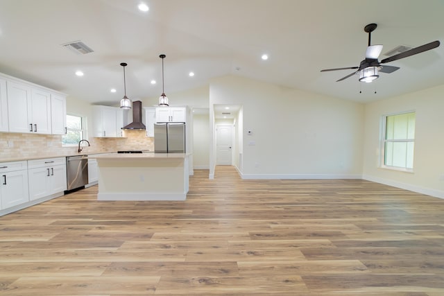 kitchen featuring wall chimney exhaust hood, white cabinetry, a center island, hanging light fixtures, and appliances with stainless steel finishes