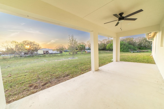 patio terrace at dusk featuring a lawn and ceiling fan