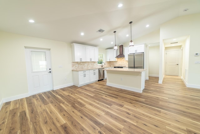 kitchen with pendant lighting, appliances with stainless steel finishes, white cabinetry, a kitchen island, and wall chimney exhaust hood