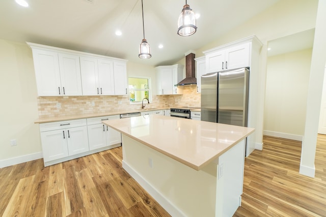 kitchen featuring wall chimney range hood, stainless steel appliances, hanging light fixtures, and white cabinets