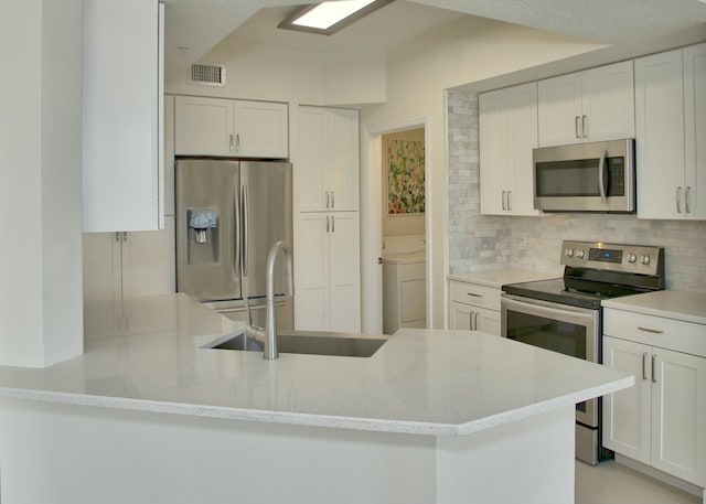 kitchen with a sink, visible vents, appliances with stainless steel finishes, backsplash, and washer / clothes dryer