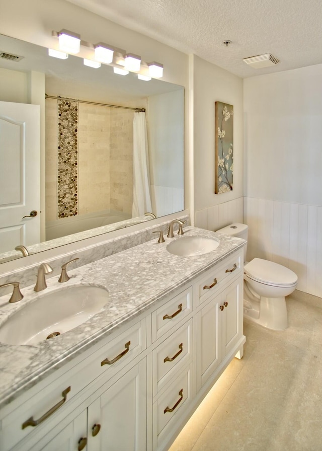 full bath featuring visible vents, wainscoting, toilet, a textured ceiling, and a sink