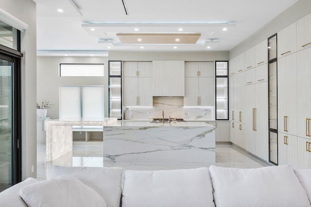 kitchen with a large island with sink, light stone countertops, sink, and decorative backsplash