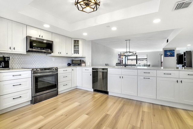 kitchen with a raised ceiling, white cabinetry, appliances with stainless steel finishes, and decorative light fixtures