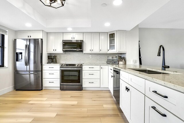 kitchen featuring sink, light hardwood / wood-style flooring, white cabinetry, stainless steel appliances, and light stone countertops