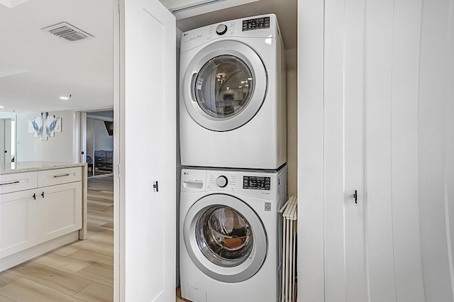 clothes washing area featuring stacked washer and dryer and light wood-type flooring