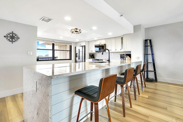 kitchen with a kitchen breakfast bar, stainless steel appliances, kitchen peninsula, and white cabinets