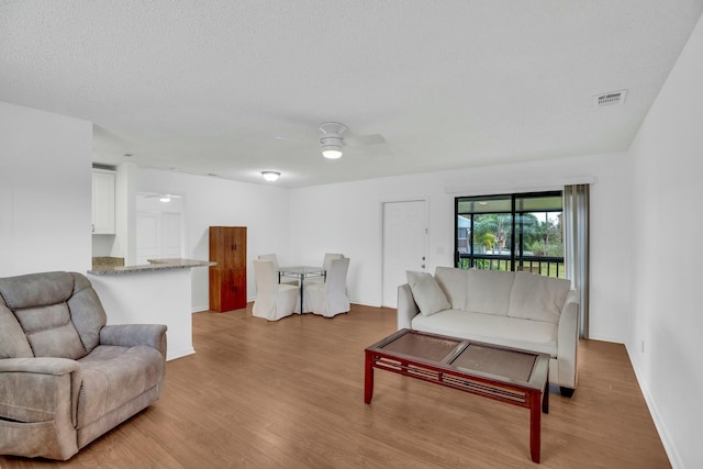 living room featuring ceiling fan, a textured ceiling, and light wood-type flooring