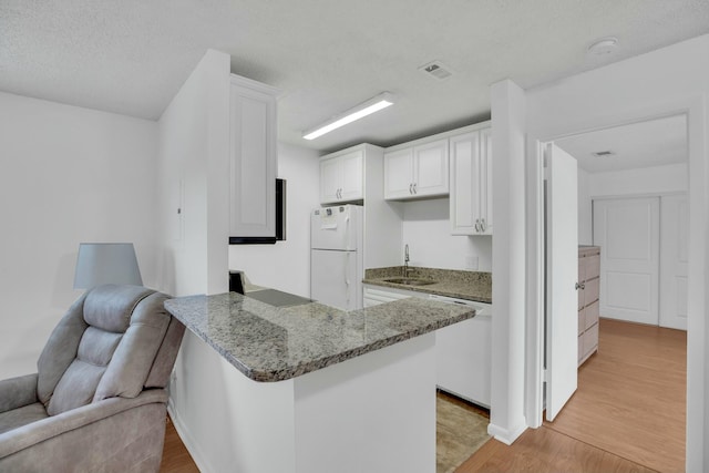 kitchen featuring kitchen peninsula, stone counters, white appliances, light hardwood / wood-style floors, and white cabinets