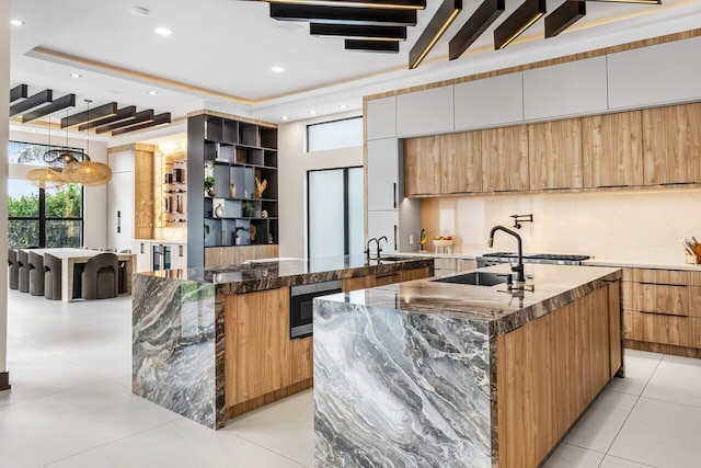 kitchen with decorative backsplash, white cabinets, decorative light fixtures, dark stone counters, and a large island with sink