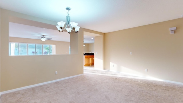 unfurnished room featuring ceiling fan with notable chandelier, baseboards, and light colored carpet