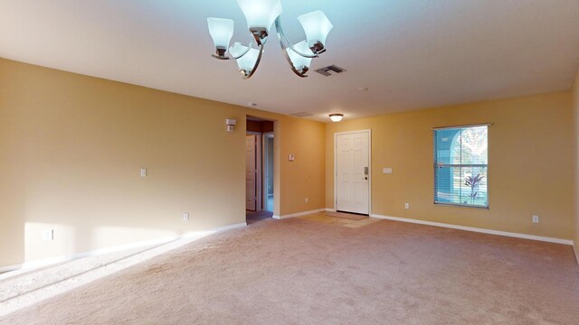 carpeted empty room featuring an inviting chandelier