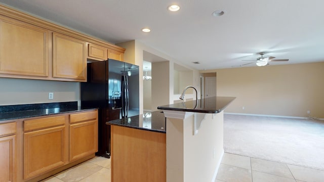 kitchen with light tile patterned flooring, open floor plan, black fridge, a center island, and dark stone countertops