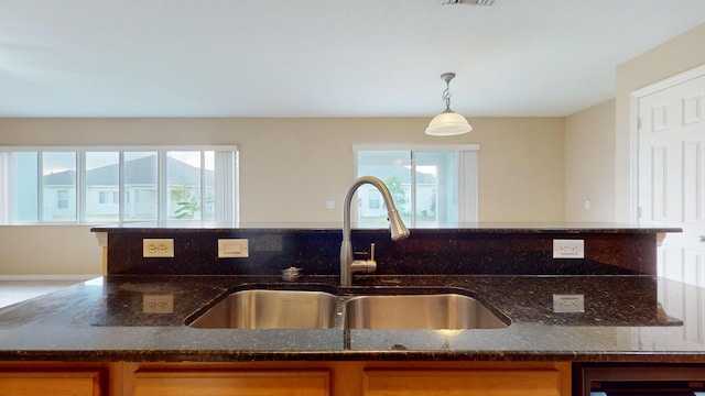 kitchen with dark stone counters, sink, hanging light fixtures, and plenty of natural light