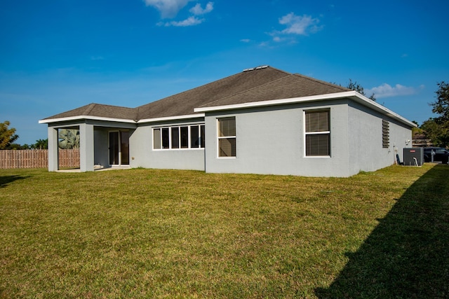 back of house featuring a shingled roof, fence, a lawn, and stucco siding