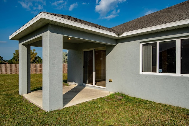 exterior space featuring a patio, roof with shingles, fence, a yard, and stucco siding