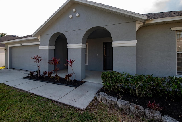 view of front of house featuring a garage, concrete driveway, roof with shingles, and stucco siding