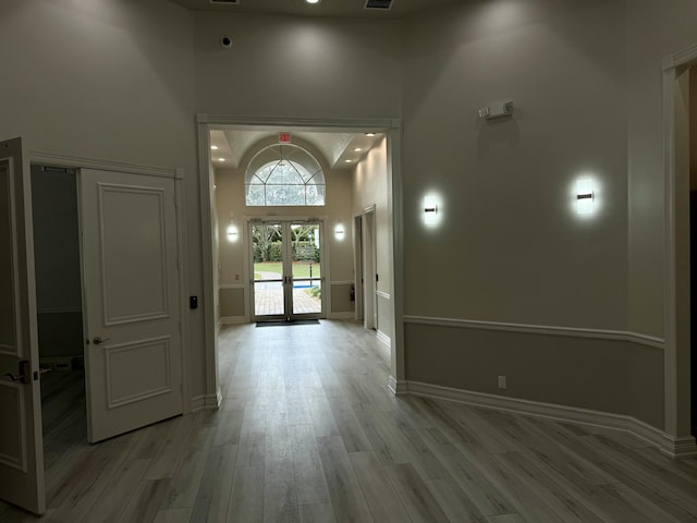 entrance foyer featuring a towering ceiling, light hardwood / wood-style flooring, and french doors