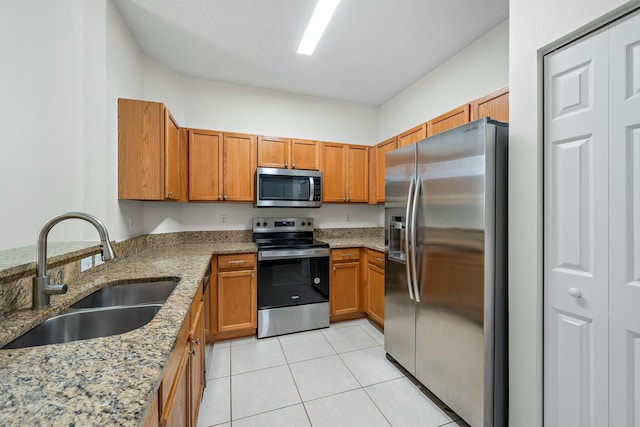 kitchen with sink, light tile patterned floors, appliances with stainless steel finishes, light stone counters, and kitchen peninsula