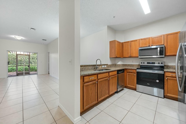 kitchen with light tile patterned flooring, sink, a textured ceiling, appliances with stainless steel finishes, and light stone countertops