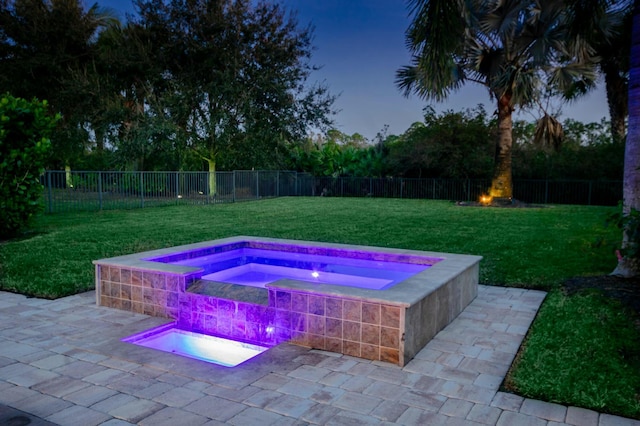 pool at dusk featuring an in ground hot tub, a yard, and a patio