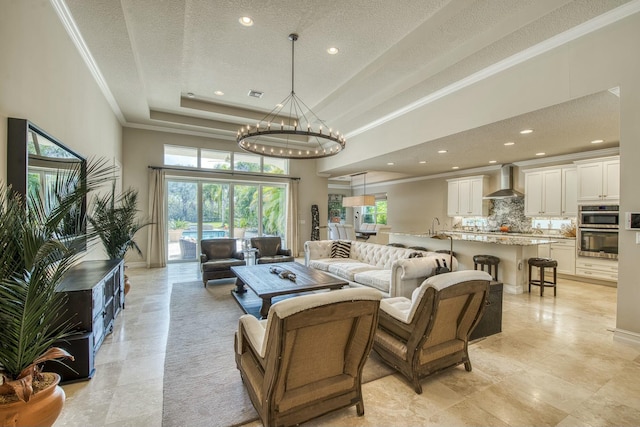 living room with a notable chandelier, ornamental molding, a raised ceiling, and a textured ceiling