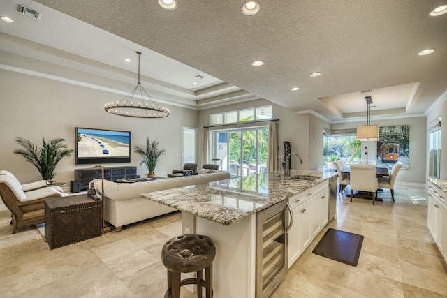 kitchen featuring wine cooler, a tray ceiling, pendant lighting, and a center island with sink