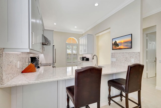 kitchen featuring white cabinets, a peninsula, light stone counters, and a kitchen breakfast bar