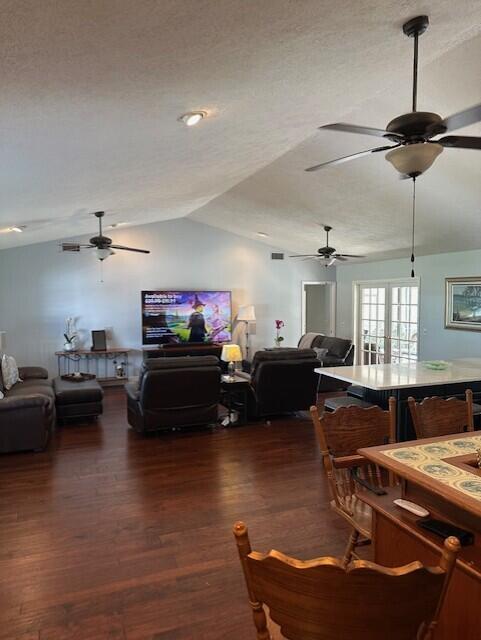 living room featuring dark wood-type flooring, vaulted ceiling, a textured ceiling, and ceiling fan