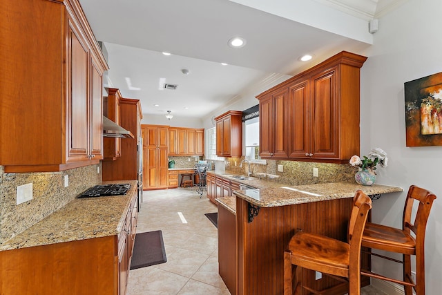 kitchen featuring stainless steel gas stovetop, light stone counters, a kitchen breakfast bar, and kitchen peninsula