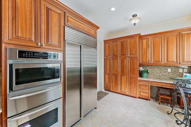 kitchen with appliances with stainless steel finishes, built in desk, backsplash, ornamental molding, and light stone countertops